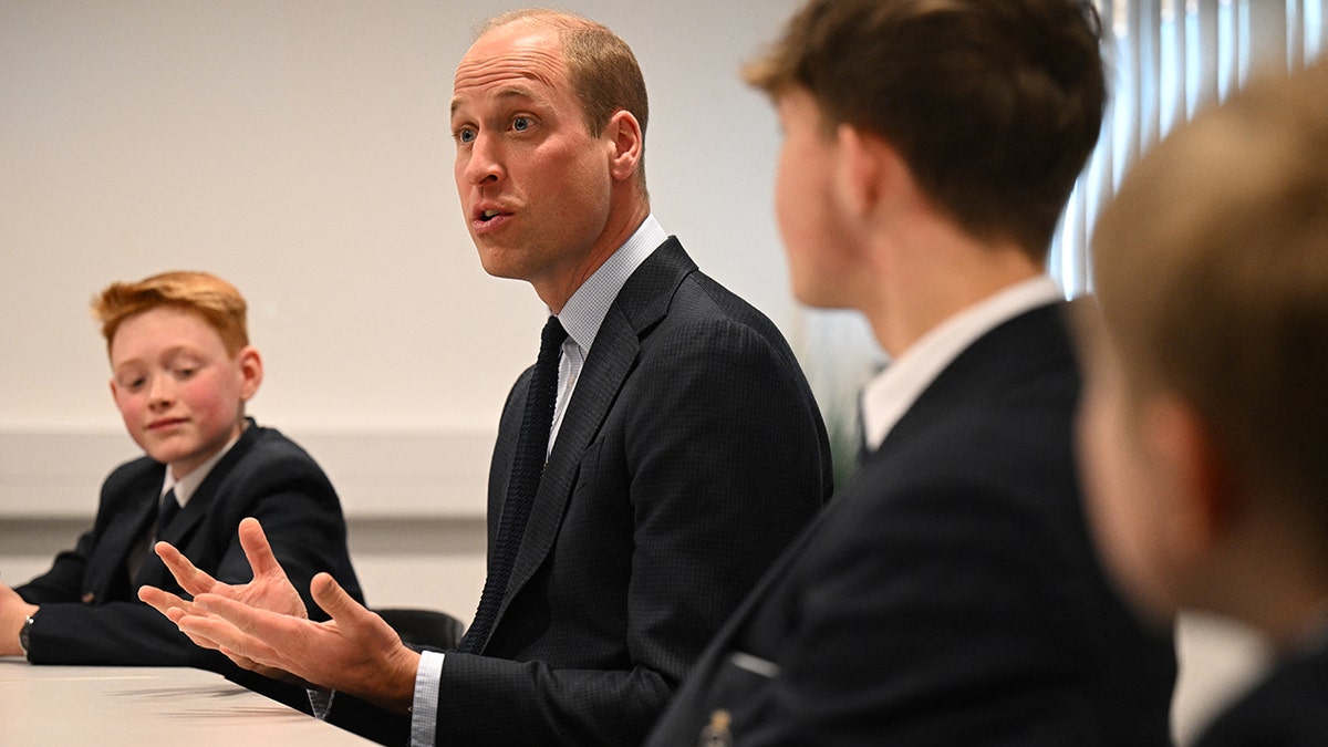 Prince William sitting adjacent to Freddie while addressing students.