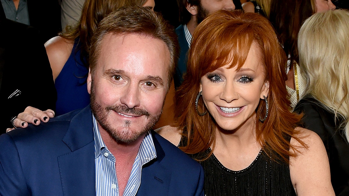 Narvel Blackstock in a blue blazer and a blue and white striped shirt smiles with Reba McEntire in a black dress at the CMAs