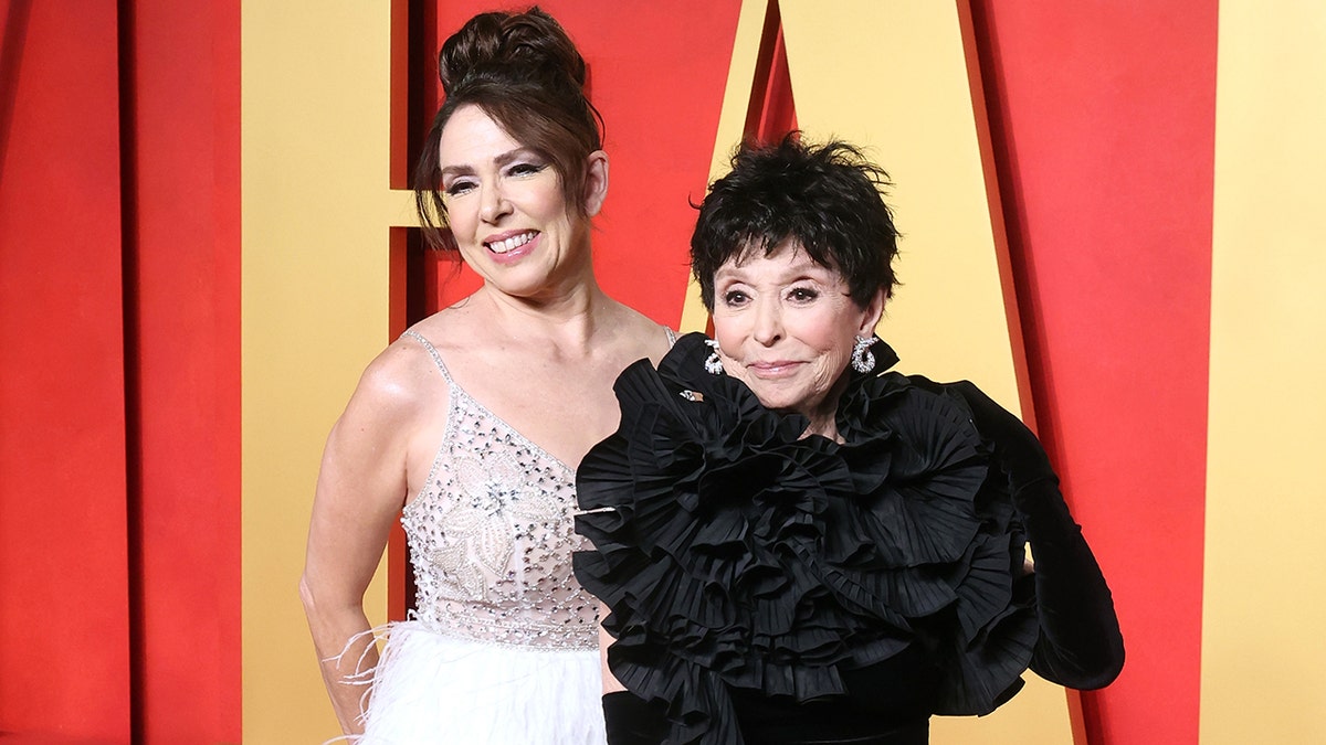 Rita Moreno in a black floral-like dress poses on the Vanity Fair carpet with daughter Fernanda in a dress with a sparkly top and white bottom