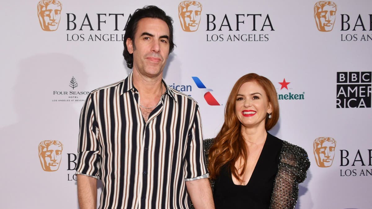 Sacha Baron Cohen and Isla Fisher smile on carpet.