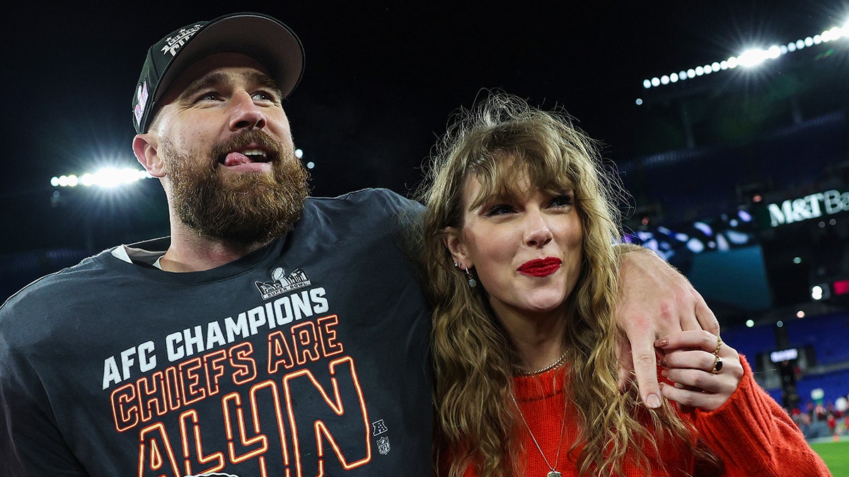 Travis Kelce after winning the AFC Championship game has his arm around Taylor Swift in a red sweater on the field