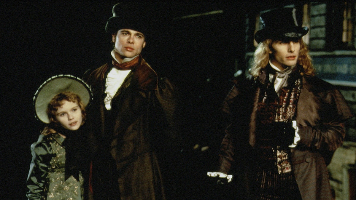 Kirsten Dunst como Claudia é segurada por Brad Pitt como Louis de Pointe du Lac em "Entrevista com um Vampiro" que está ao lado de Tom Cruise como Lestat de Lioncourt