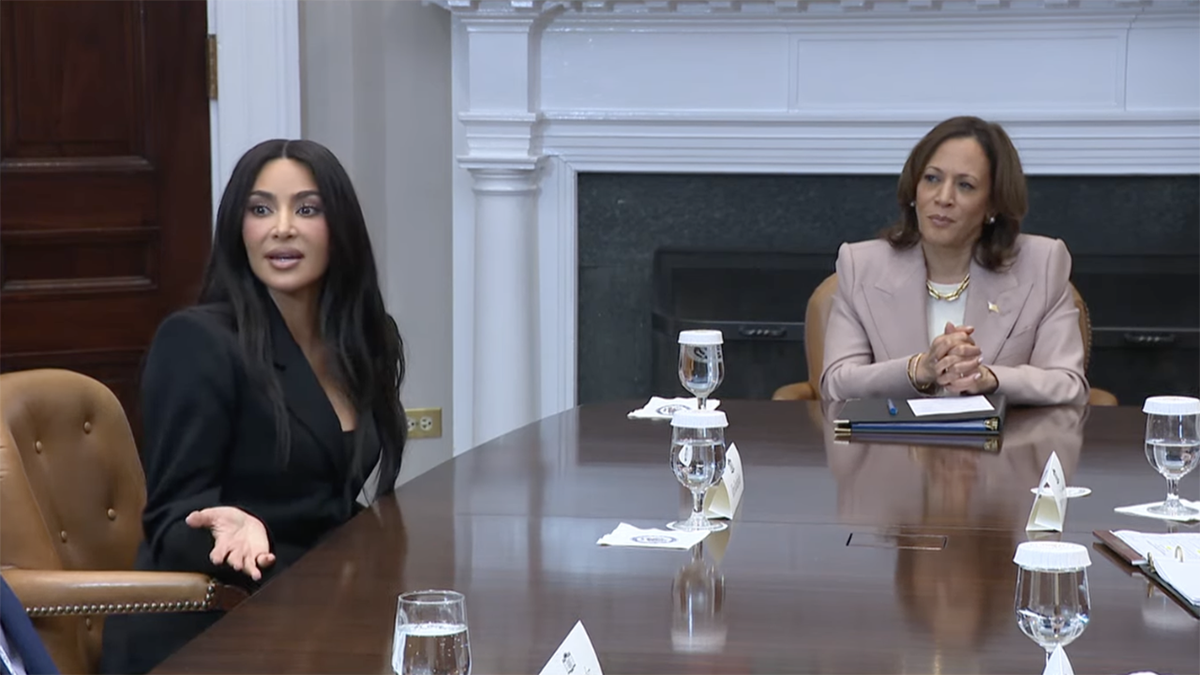 Kim Kardashian in a black suit sits around a table with Vice President Kamala Harris in a light mauve suit