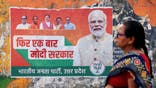 A woman walks past an election campaign poster of the Bharatiya Janata Party (BJP) featuring their leader and India's Prime Minister Narendra Modi (R), along a street in Varanasi on March 24, 2024, ahead of the country's upcoming general elections. (Photo by NIHARIKA KULKARNI/AFP via Getty Images)