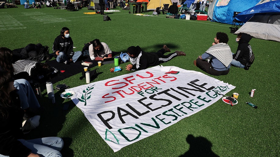 Personas sentadas junto a una pancarta en un campamento de protesta en apoyo a los palestinos