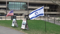 An American and Israeli flag wave in the breeze on either side of signs that discuss IDF soldiers and people kidnapped by Hamas.