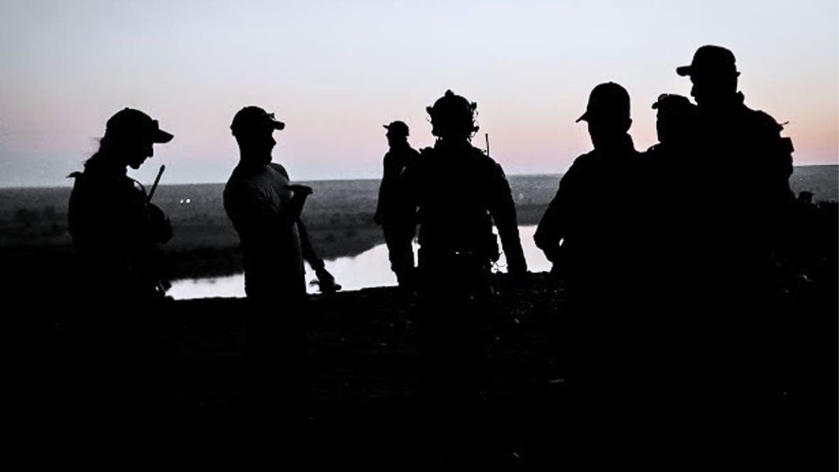 Group of seven U.S. Army soldiers in a huddle outside at dusk