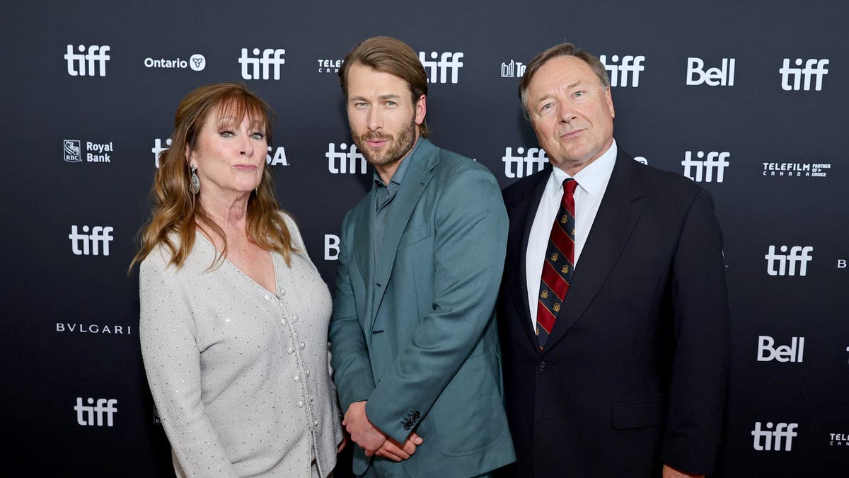 Glen Powell posing with his parents on the red carpet.