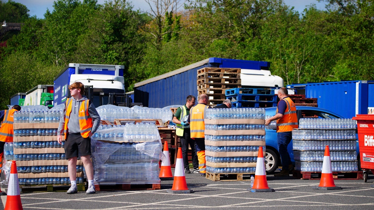 Trabajadores con chalecos naranjas rodean palés llenos de agua embotellada para que la gente se acerque al aparcamiento Broadsands en Paignton, Inglaterra.