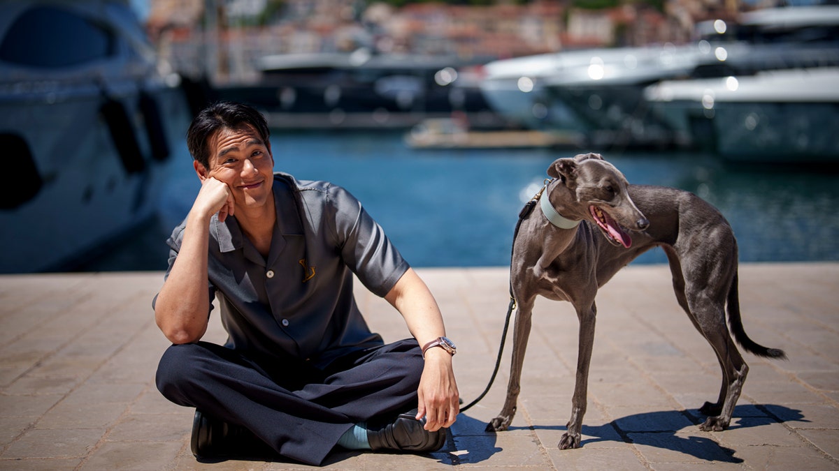 Eddie Peng poses with his dog Xin on a pier in front of boats during an interview for the film 'Black Dog' at the 77th international film festival,.