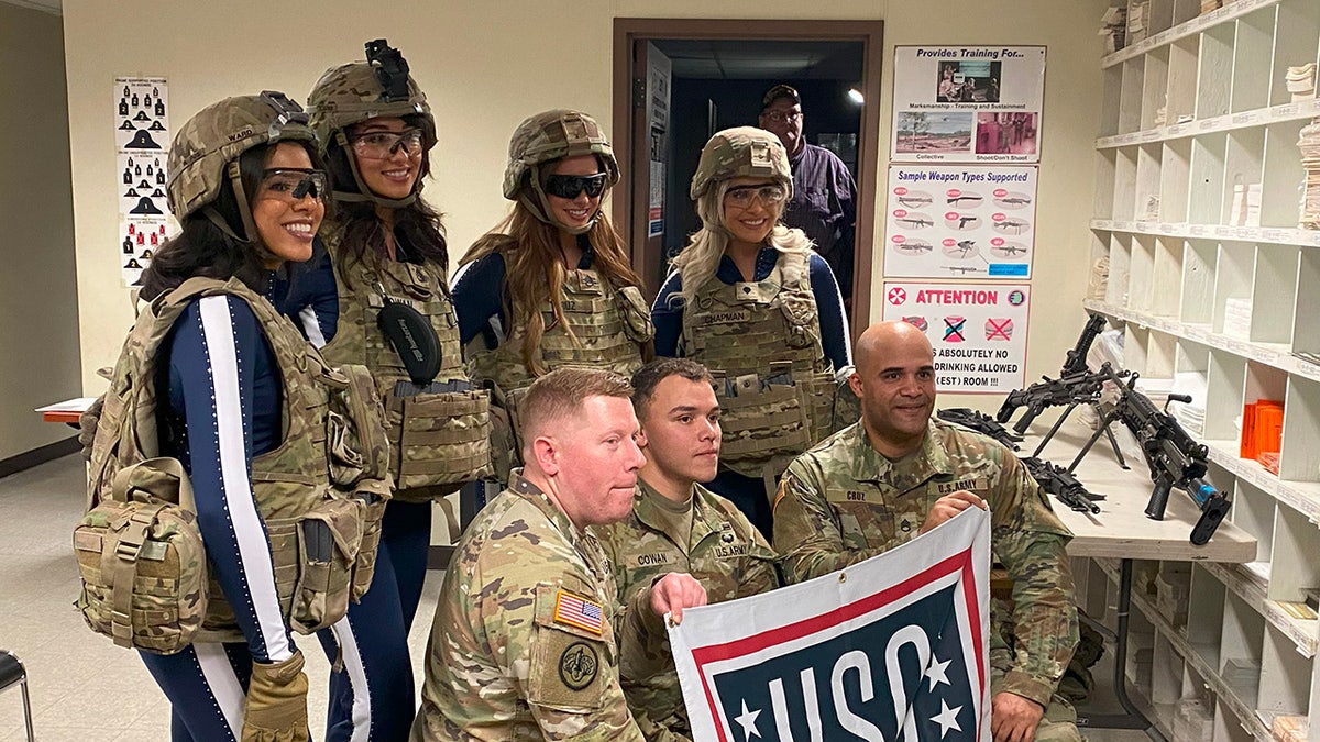 A group of Dallas Cowboys Cheerleaders in uniform with servicemen holding a USO sign