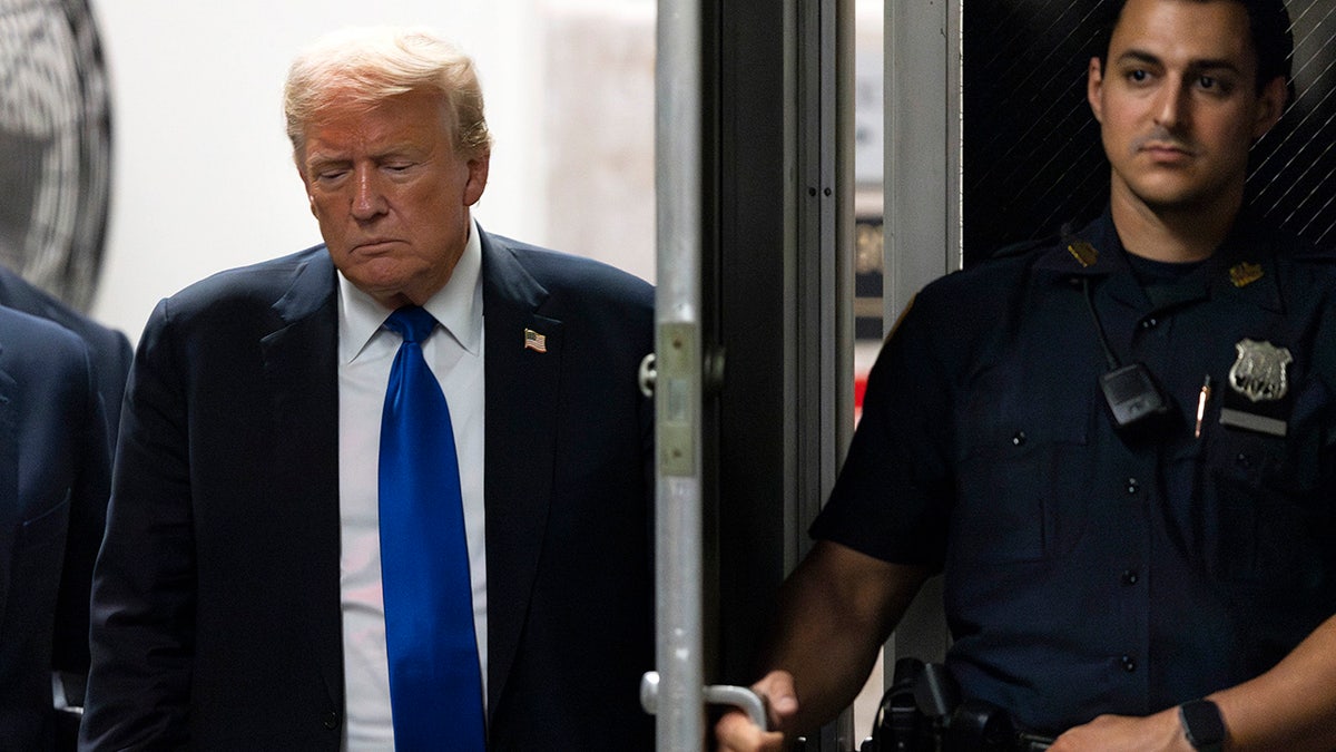 Donald Trump in dark coat, blue tie, walking through door