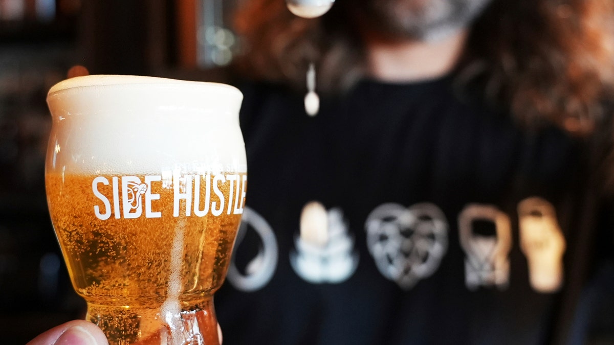 Mitchell Dougherty, the brewmaster at Side Hustle Brews and Spirts, pours a pint of beer into a glass that reads "SHIDE HUSTLE" at his brew pub in Abu Dhabi, United Arab Emirates