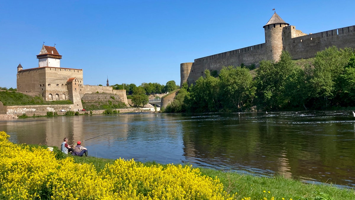 Men fish near the fortresses of Narva, left, in Estonia, and Ivangorod, right, in Russia, in front of yellow flowers on the Narva River.