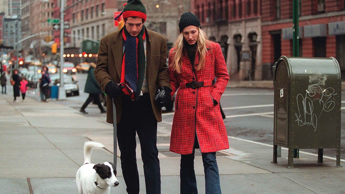 John F. Kennedy Jr. and Carolyn Bessette-Kennedy walking outside with their dog.