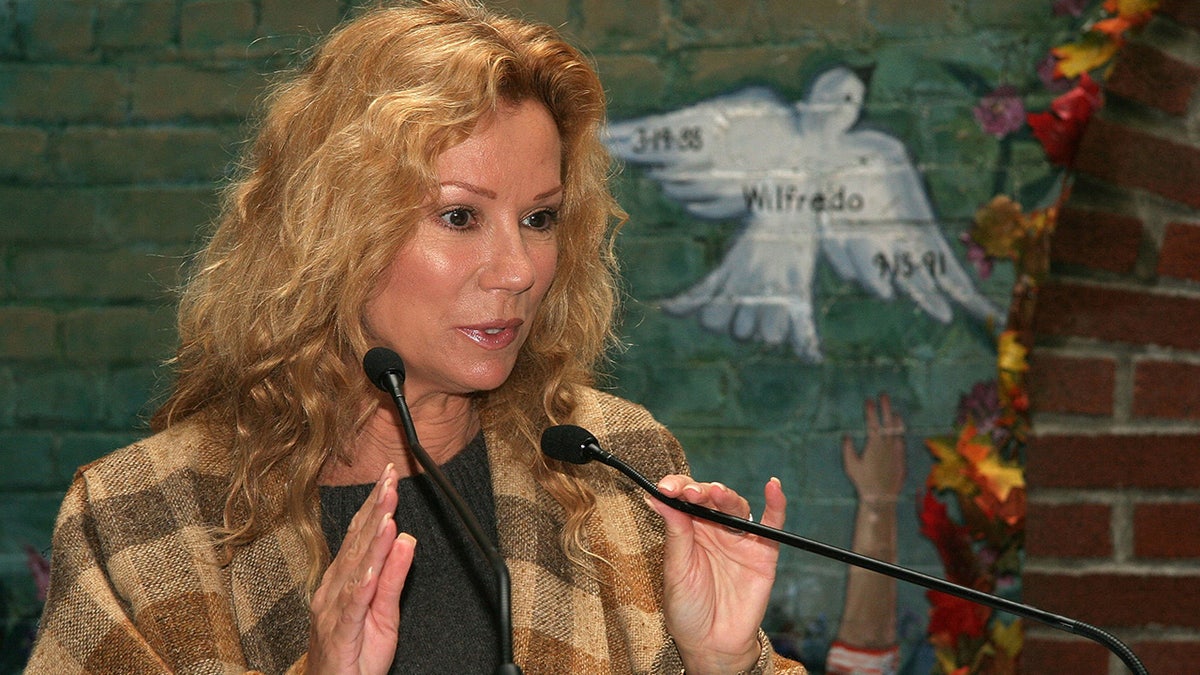 Kathie Lee Gifford speaking to a mic next to a painting of a dove