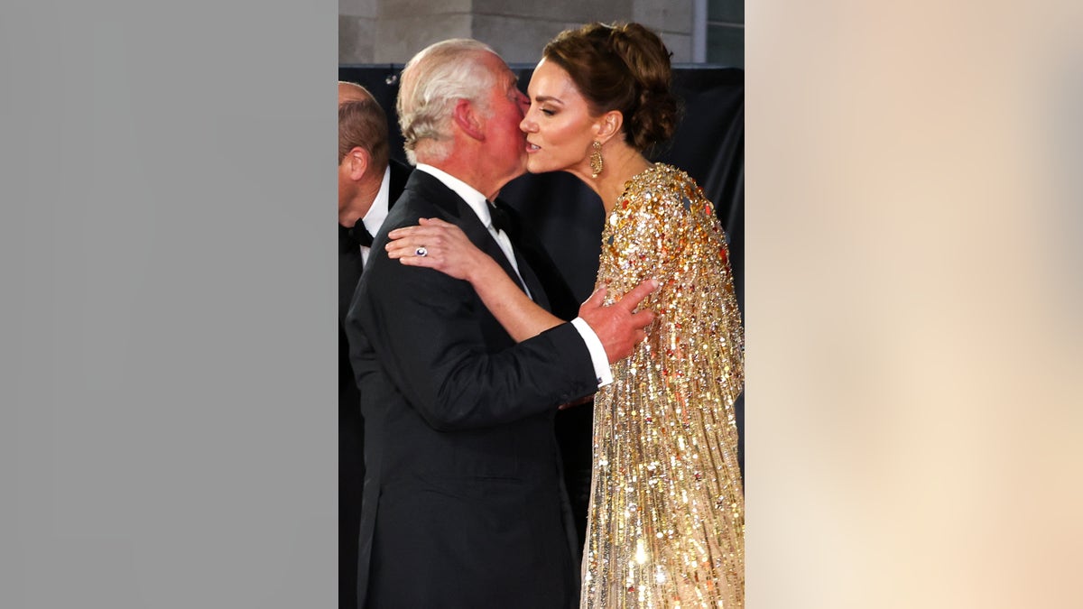 Kate Middleton wearing a gold sparkling dress giving King Charles III a kiss on the cheek.