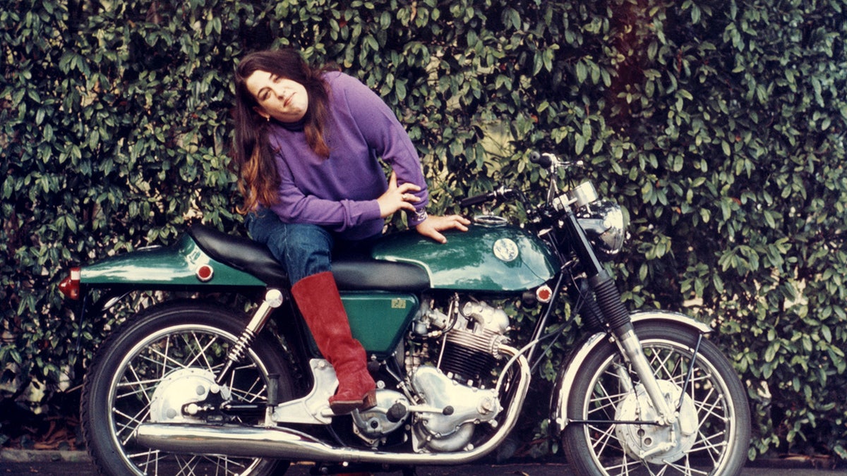 Cass Elliot smiling and sitting on top of a motorcycle