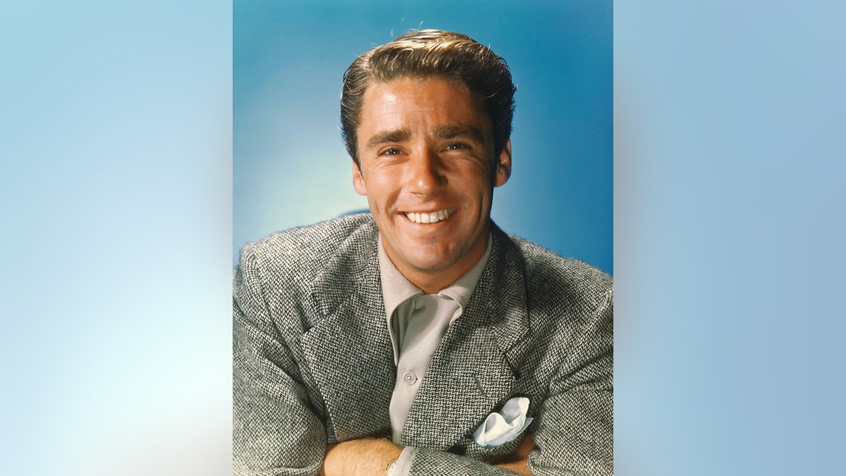 A close-up photo of Peter Lawford smiling in a grey suit