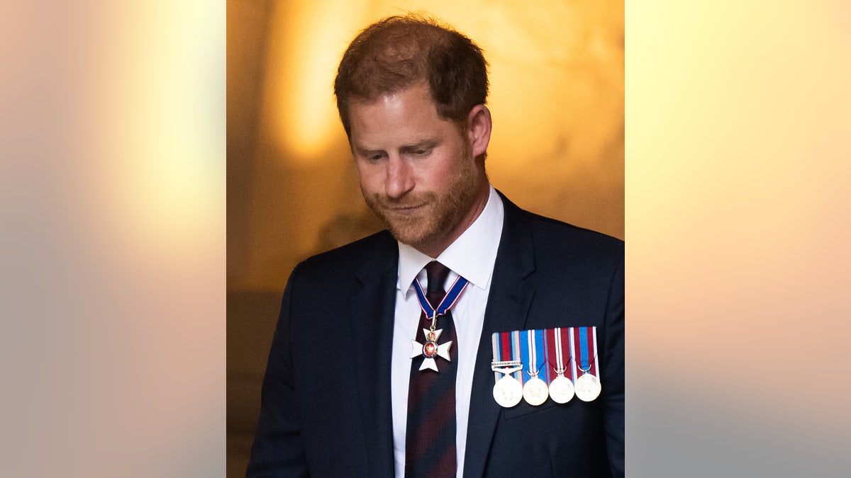 Prince Harry looking down while wearing a suit with medals