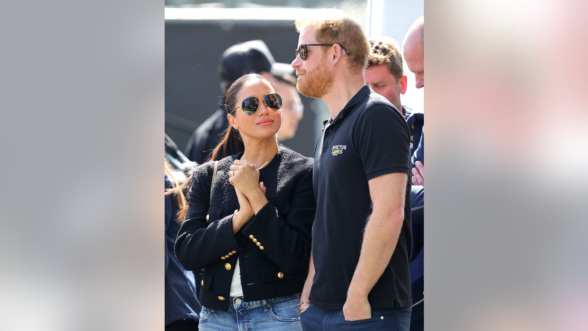 Meghan Markle with her hands clasp together as she looks up at Prince Harry