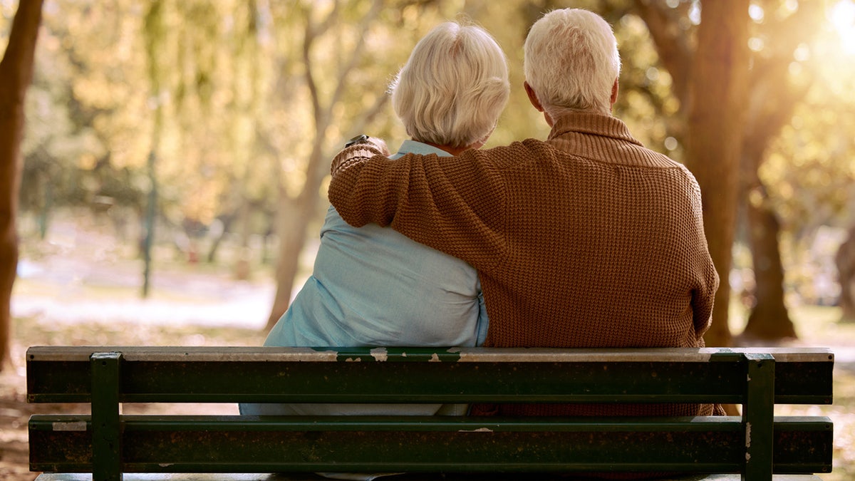 An elderly couple sits on a bench together.