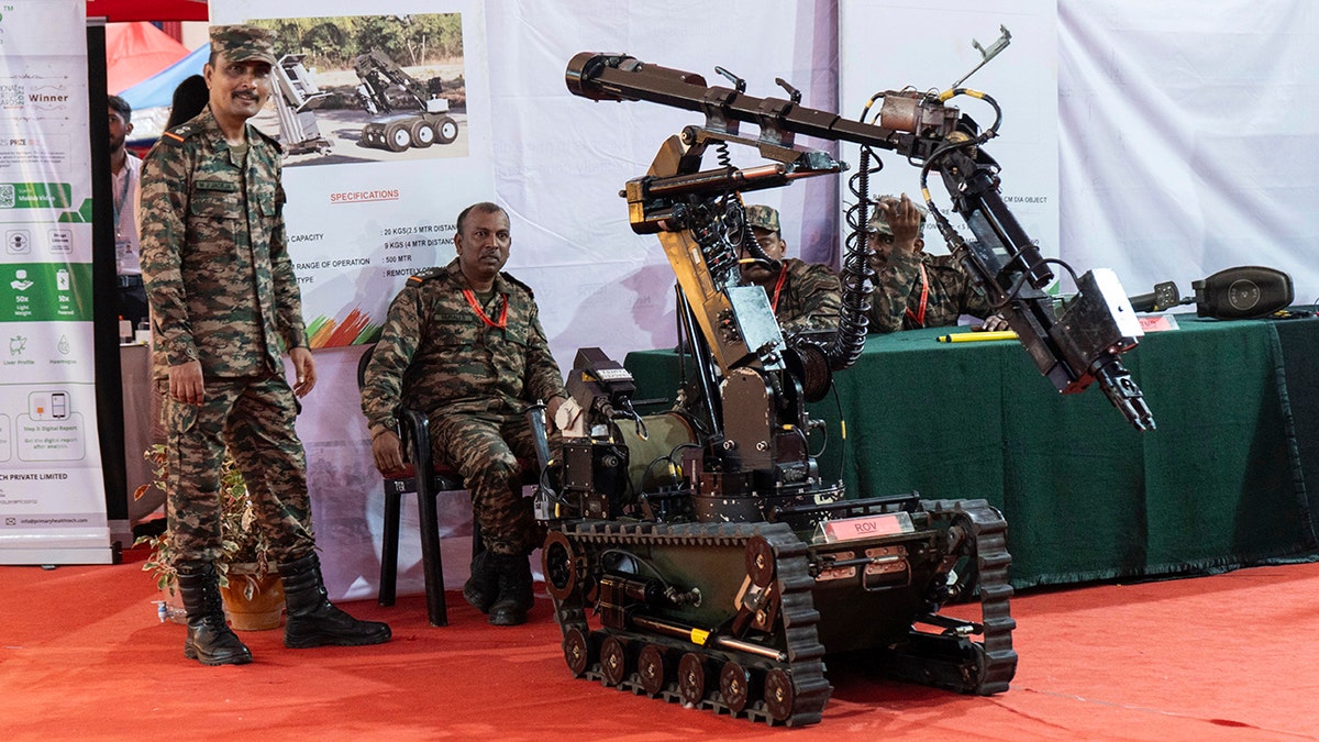 Two men in fatigues stand beside a robot at a trade fair