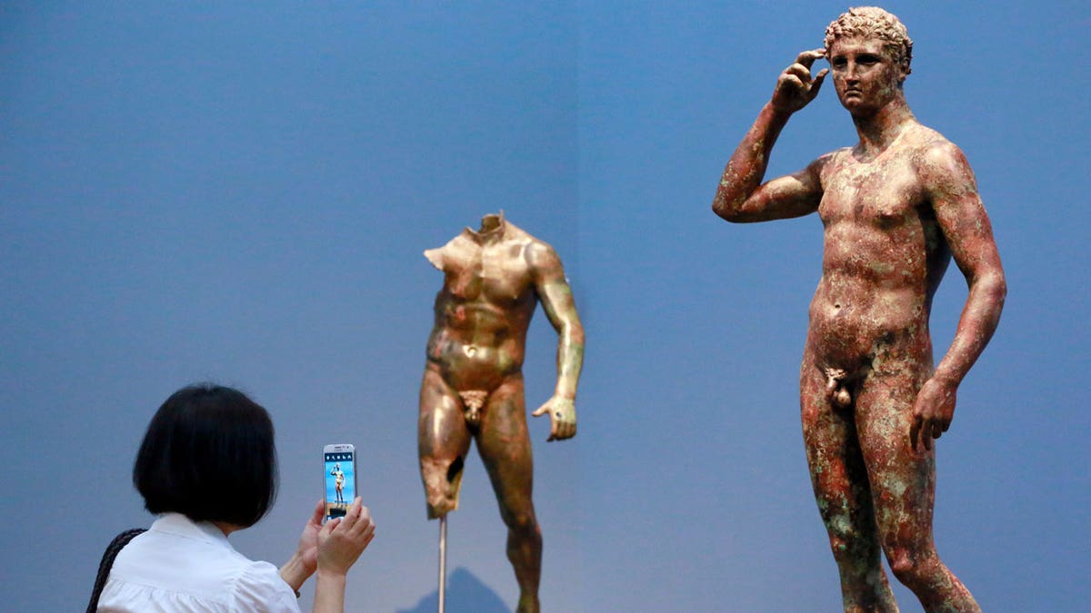 Reporter Sookee Chung takes a photo of a sculpture titled "Statue of a Victorious Youth, 300-100 B.C." at the J. Paul Getty Museum in Los Angeles