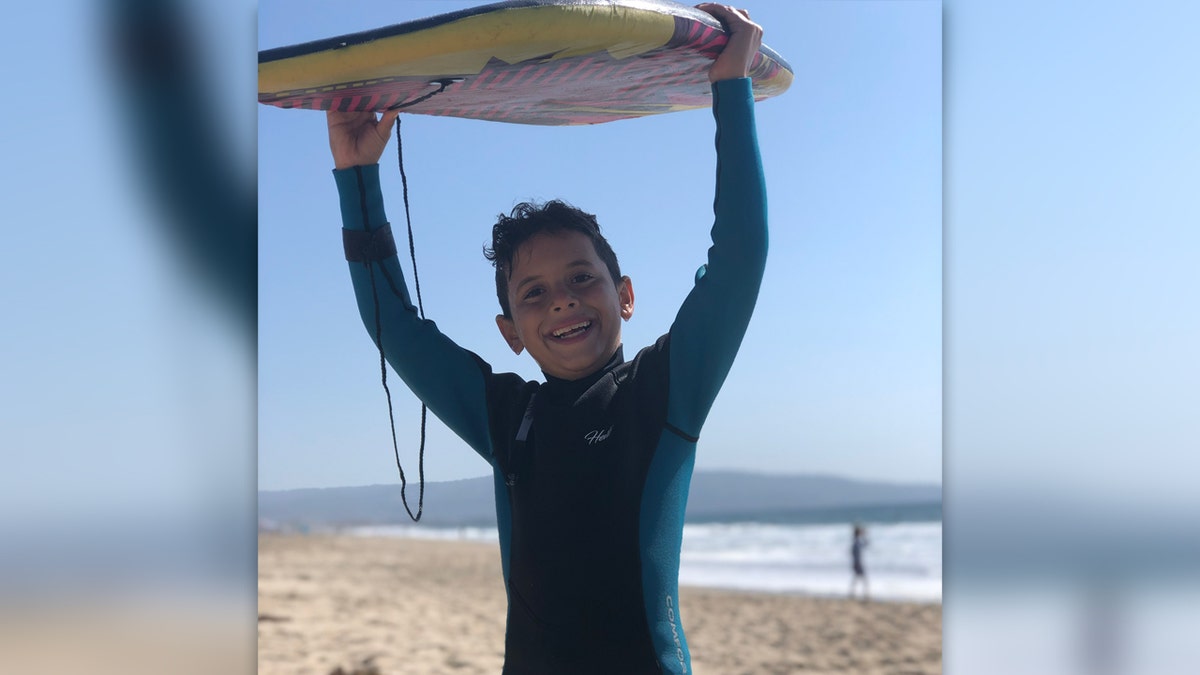 Jacob Iskander at beach holding body board above his head and wearing a wetsuit