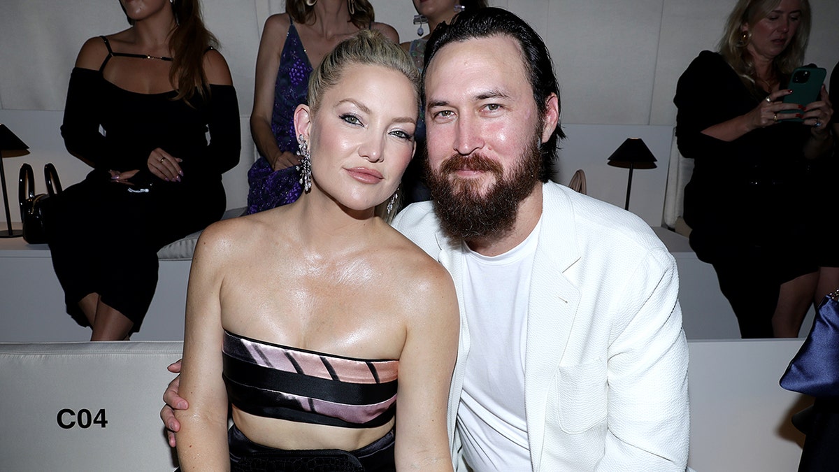Kate Hudson in a black two piece outfit leans against fiancé Danny Fujikawa at the Armani Privé show