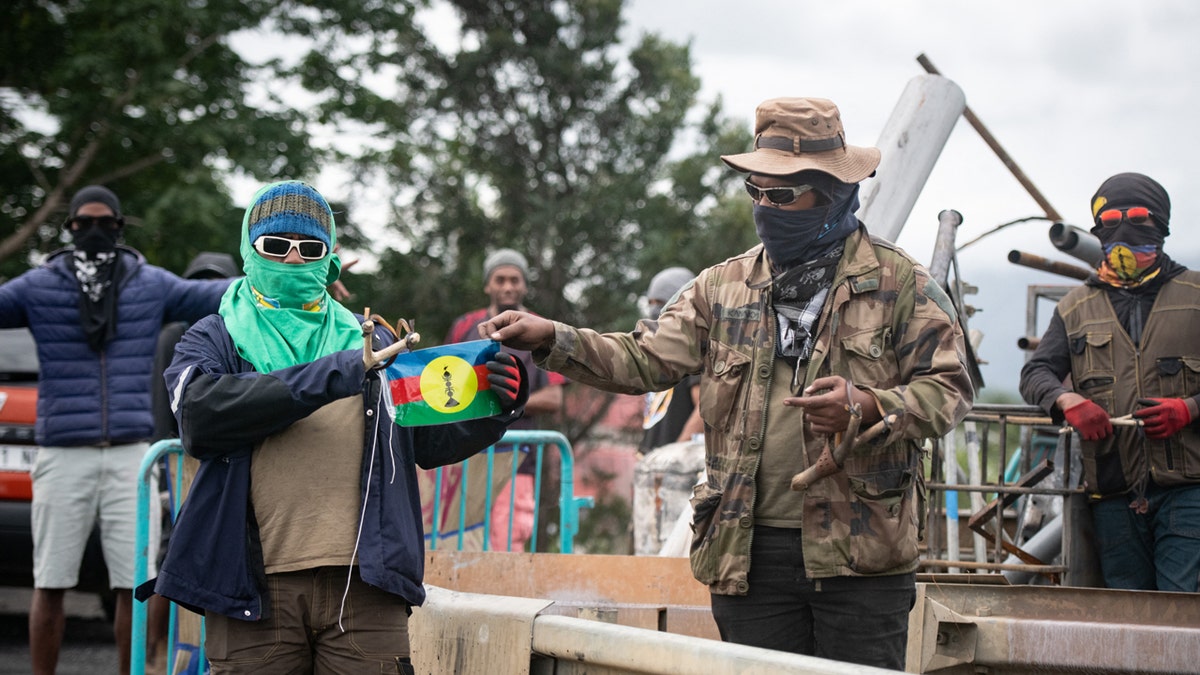 Bystanders hold a flag of the Socialist Kanak National Liberation Front on a roadblock in Ducos, New Caledonia