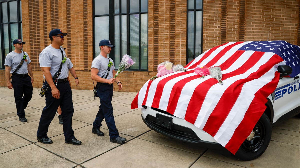 Charlotte firefighters from Engine 7 bring flowers to a flag-covered Charlotte-Mecklenburg police vehicle