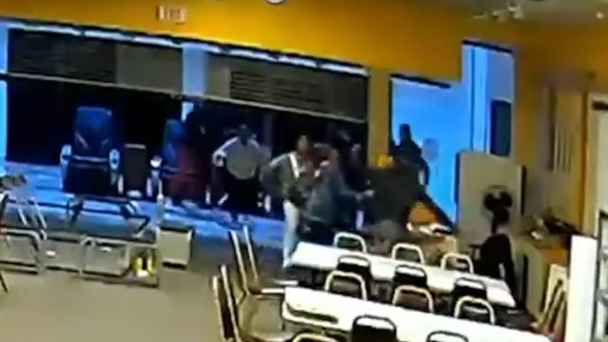 Victim is on the ground behind a table as attackers punch and kick him on the ground