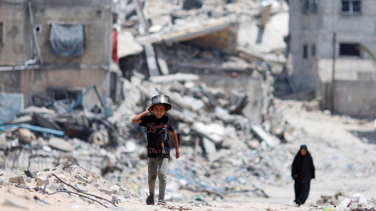 Palestinians walk by houses destroyed in an Israeli strike