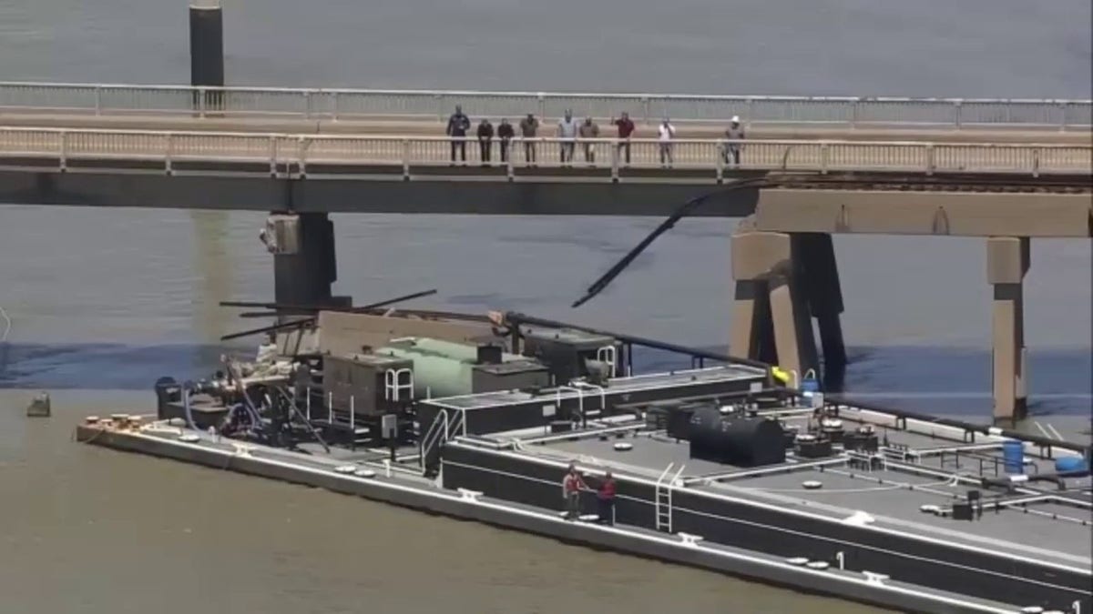Several people look down at a barge on the Pelican Island Bridge