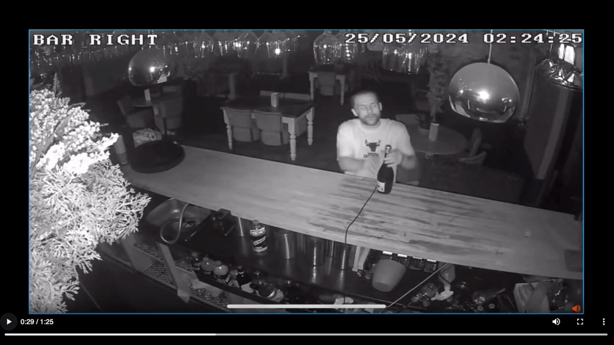 A burglar in a Chicago Bulls T-shirt pops a bottle of proseccor in a still taken from security video