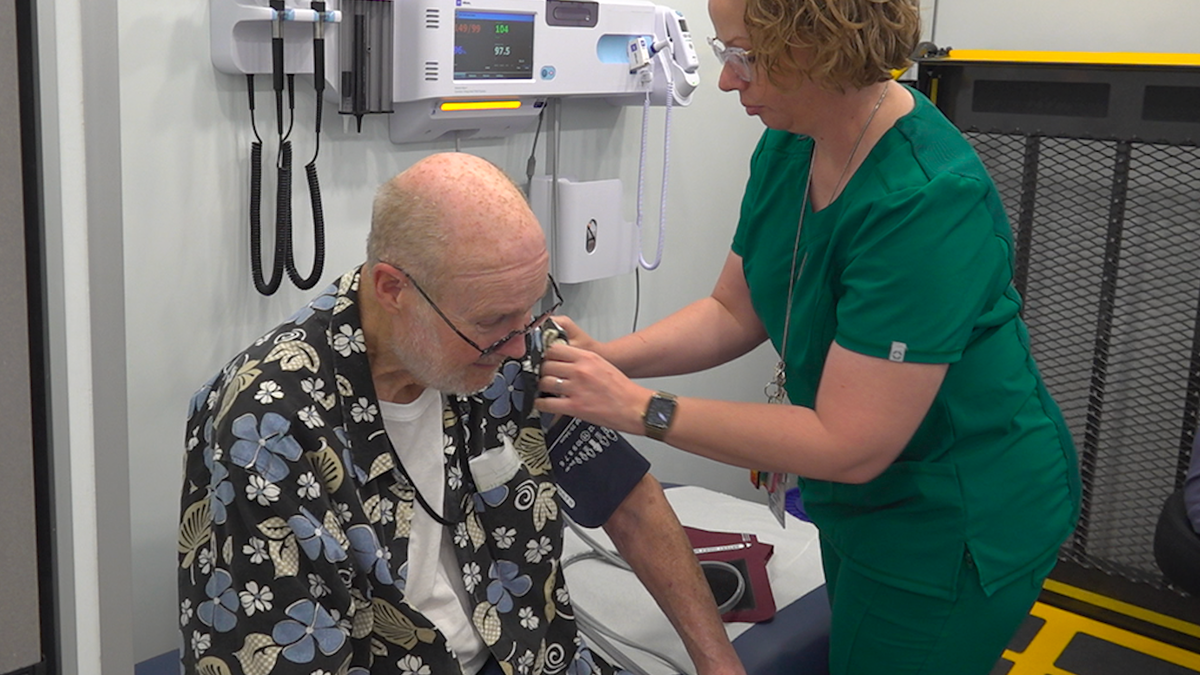 A man sits as a nurse puts on his blood pressure cuff