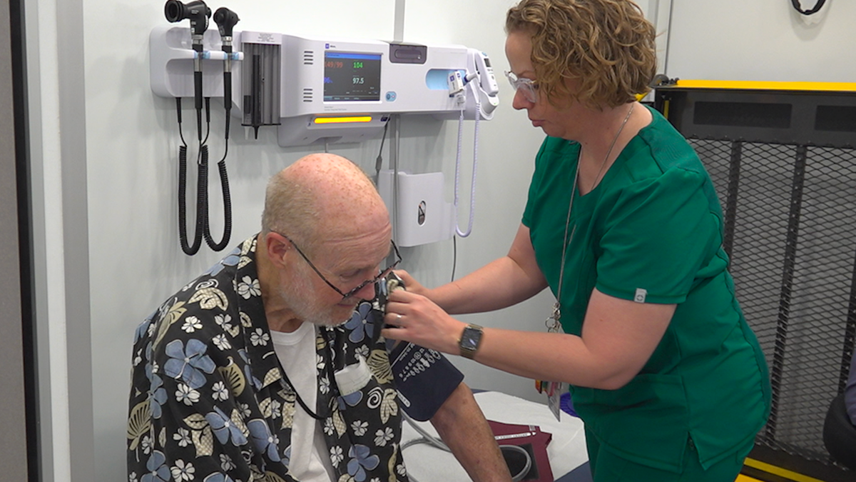 A man sits as a nurse puts on his blood pressure cuff