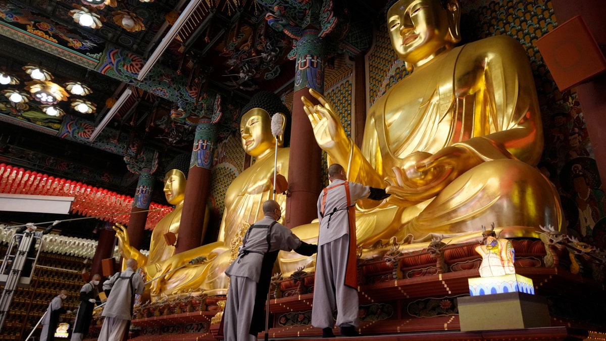 Buddhists monks clean giant, gold Buddha statues