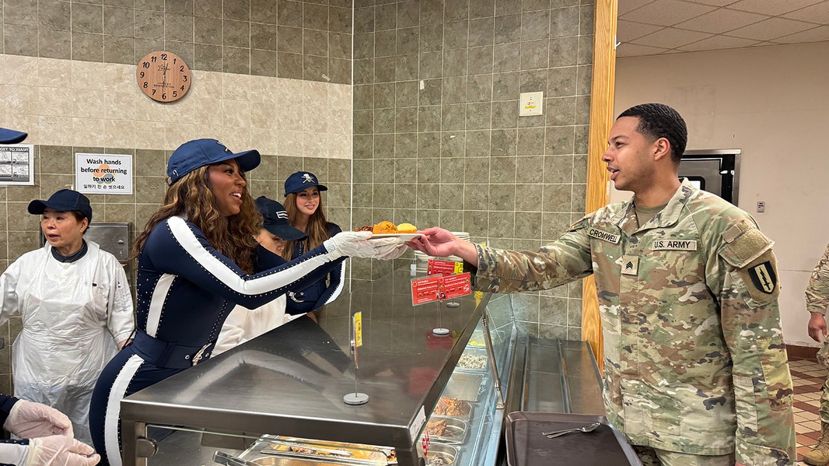 A Dallas Cowboy cheerleader handing food to a serviceman at a cafeteria