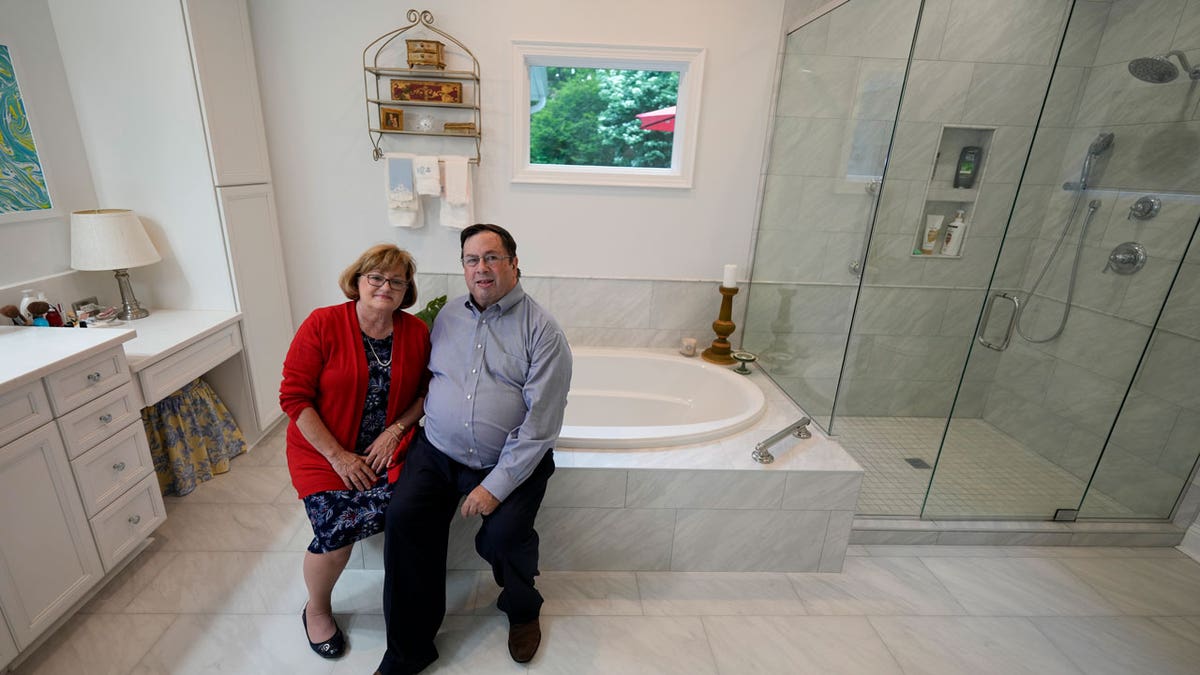 Gene and Sallie Carr pose for a picture in their recently remodeled bathroom with extra features for accessibility, like a walk-in shower and a handle on the bathtub.