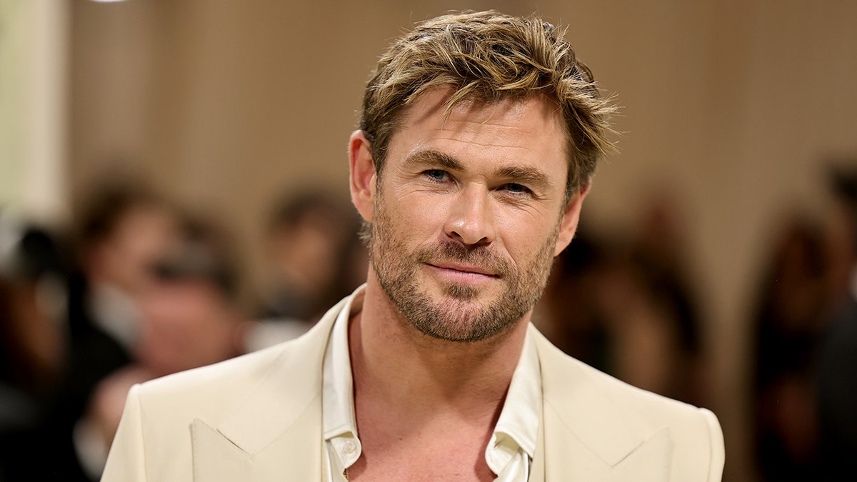 Chris Hemsworth in a light tan suit poses on the Met Gala carpet