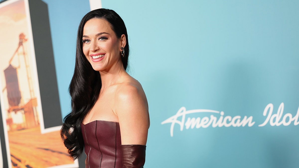 Katy Perry in a maroon leather dress and matching gloves smiles on the carpet for an "American Idol" event