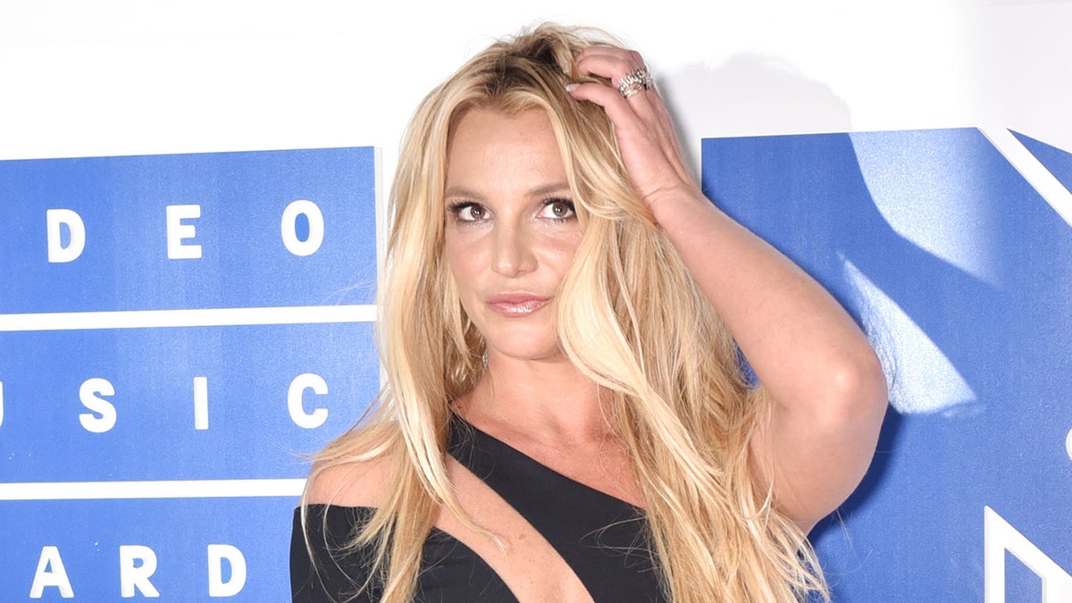 Singer Britney Spears wears achromatic trim retired dress connected reddish carpet.