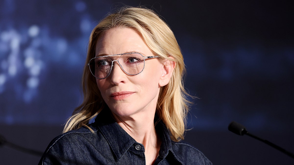 Cate Blanchett with transparent aviator glasses looks to her right on a panel at Cannes