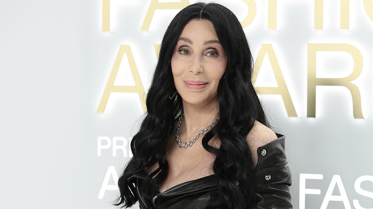 Cher in a black off the shoulder off the shoulder leather outfit soft smiles on the carpet
