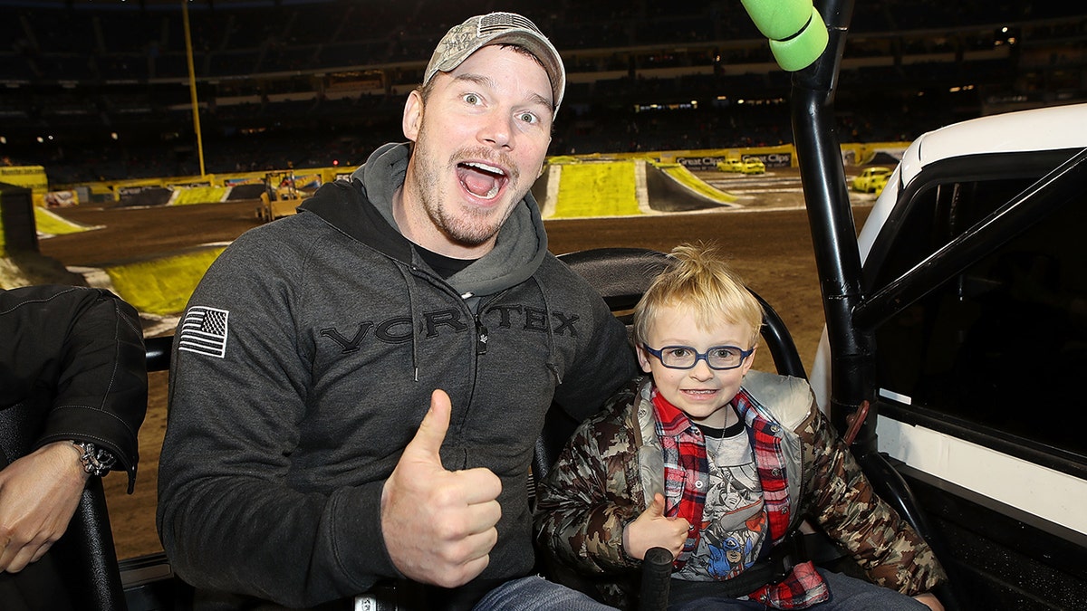 Chris Pratt in a sweatshirt gives a thumbs up with his son Jack at Monster Jam event