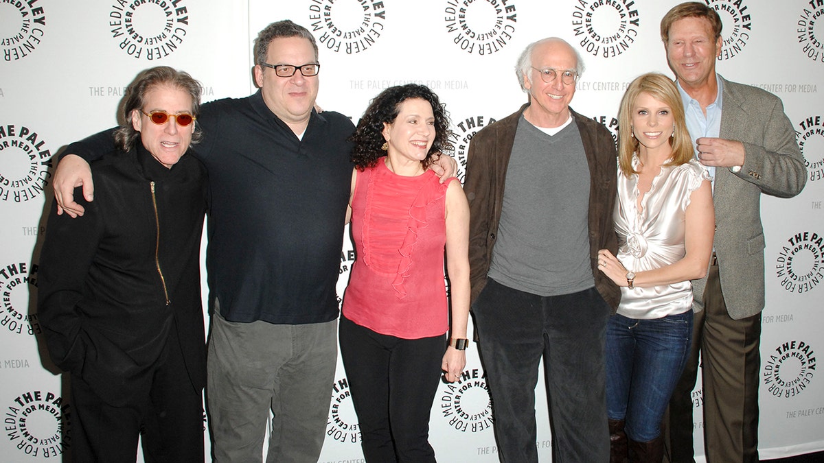 Larry David and cast members posing on the red carpet at an event.