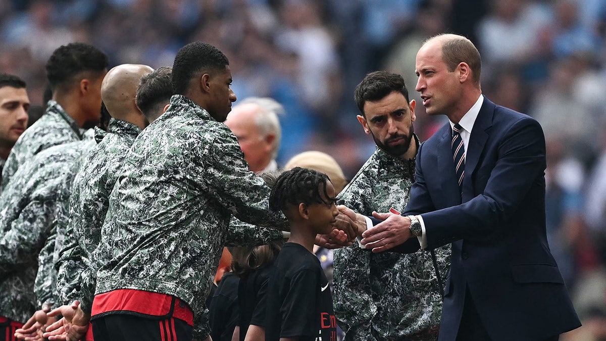 Prince William greeting several men on the field