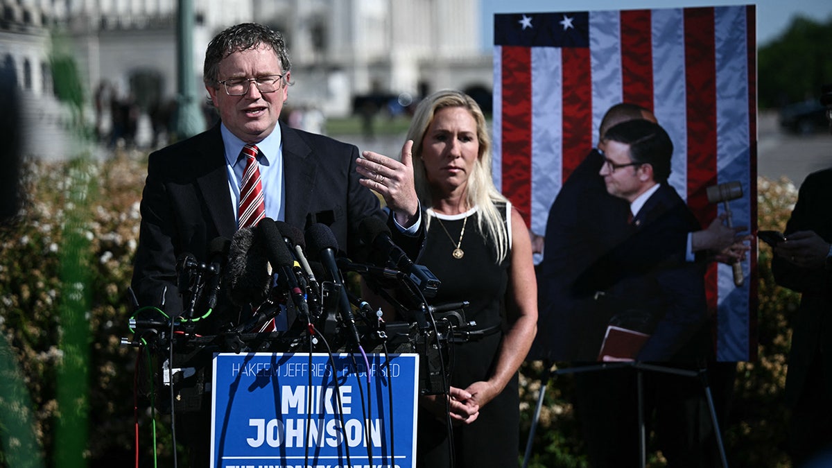 Massie and Greene in front of a photo of Johnson hugging Jeffries